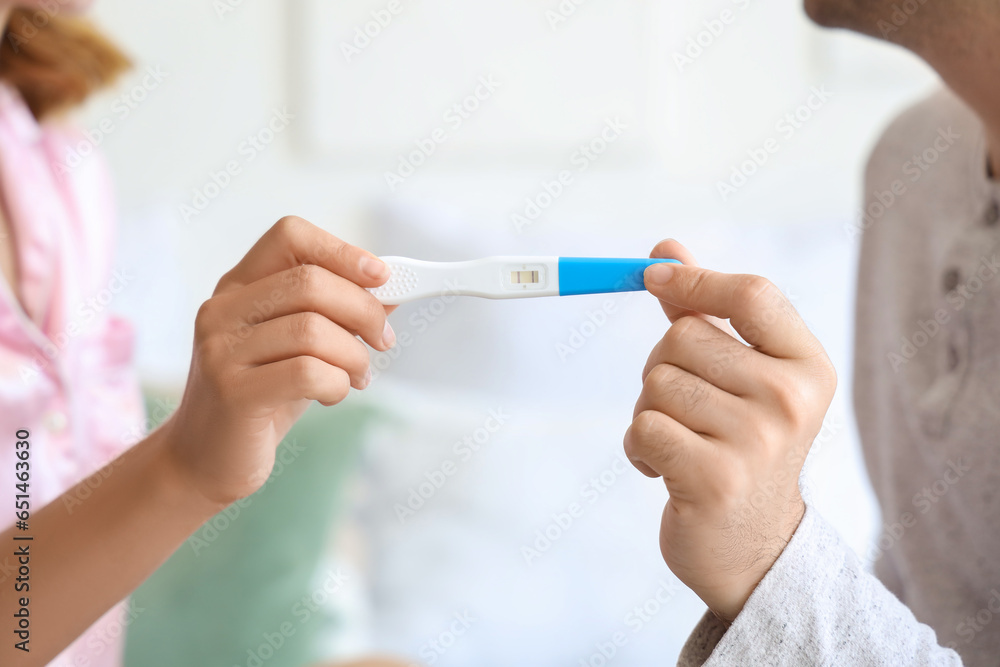 Happy young couple with pregnancy test in bedroom, closeup