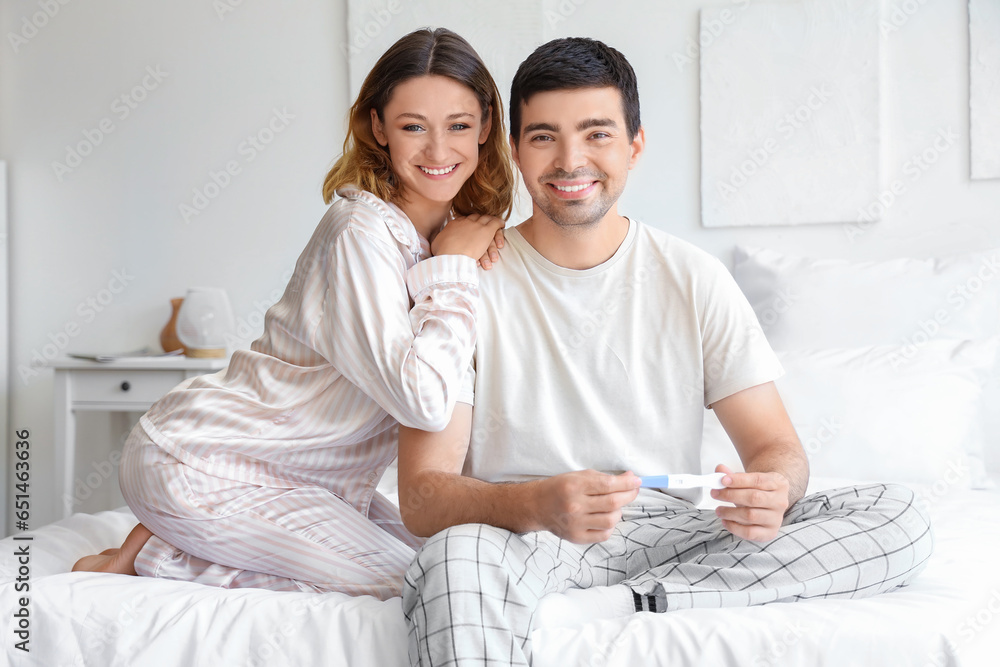 Happy young couple with pregnancy test in bedroom