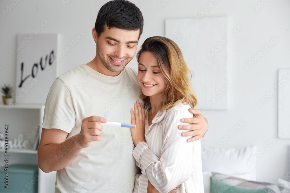 Happy young couple with pregnancy test in bedroom