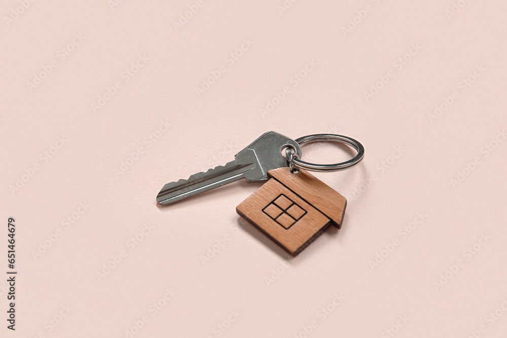 Key with trinket in house shape on pink background. Concept of buying real estate