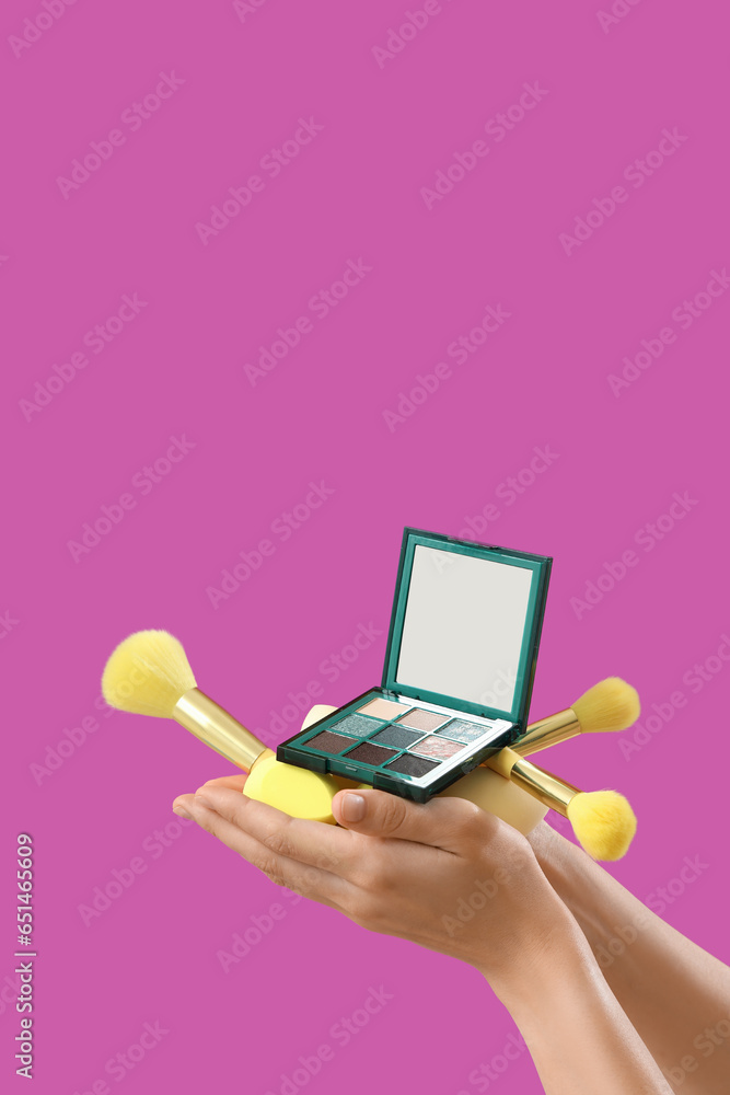 Woman with makeup brushes, sponges and eyeshadows on purple background