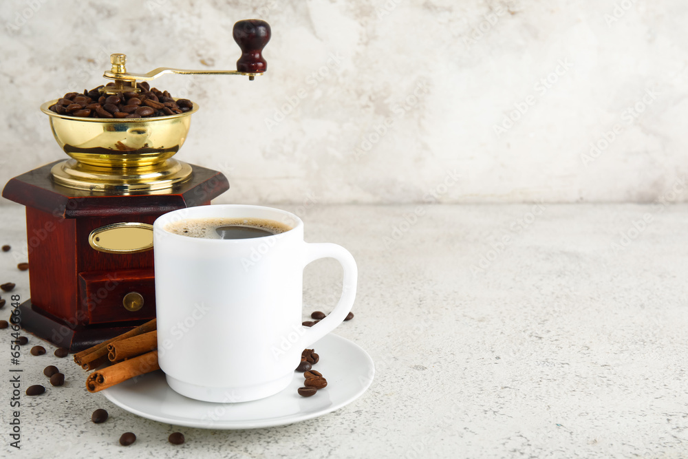 Cup of tasty coffee with cinnamon and grinder on light background