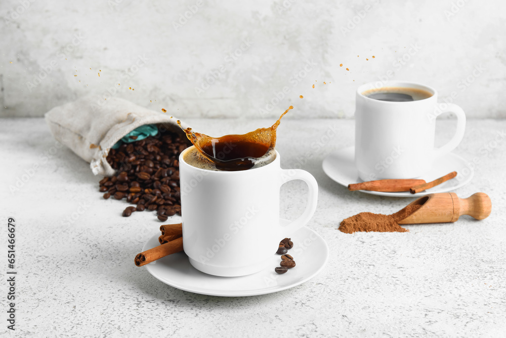 Cup of tasty coffee with splashes and cinnamon on light background