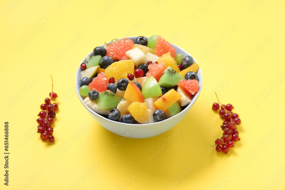 Bowl with fresh fruit salad on yellow background