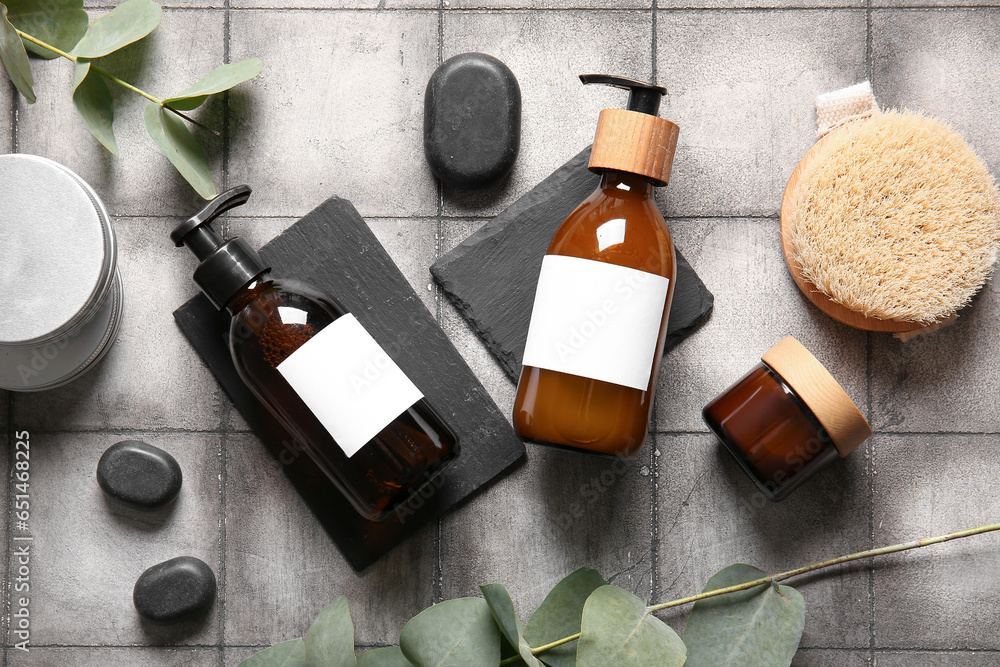 Bottles of shampoo, spa stones, brush and cosmetic products on grey tile background