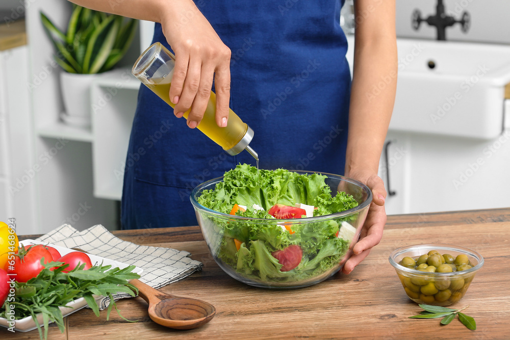 Woman adding olive oil into bowl with tasty salad at table in kitchen