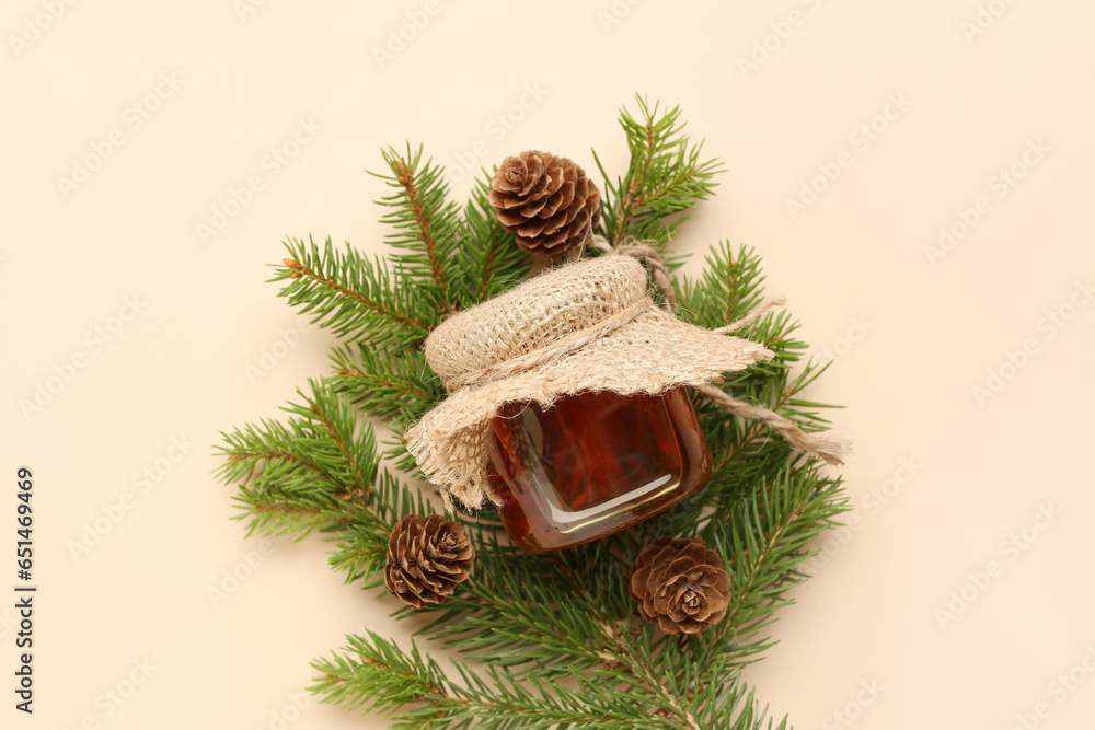 Jar with tasty honey, fir tree branch and pine cones on beige background