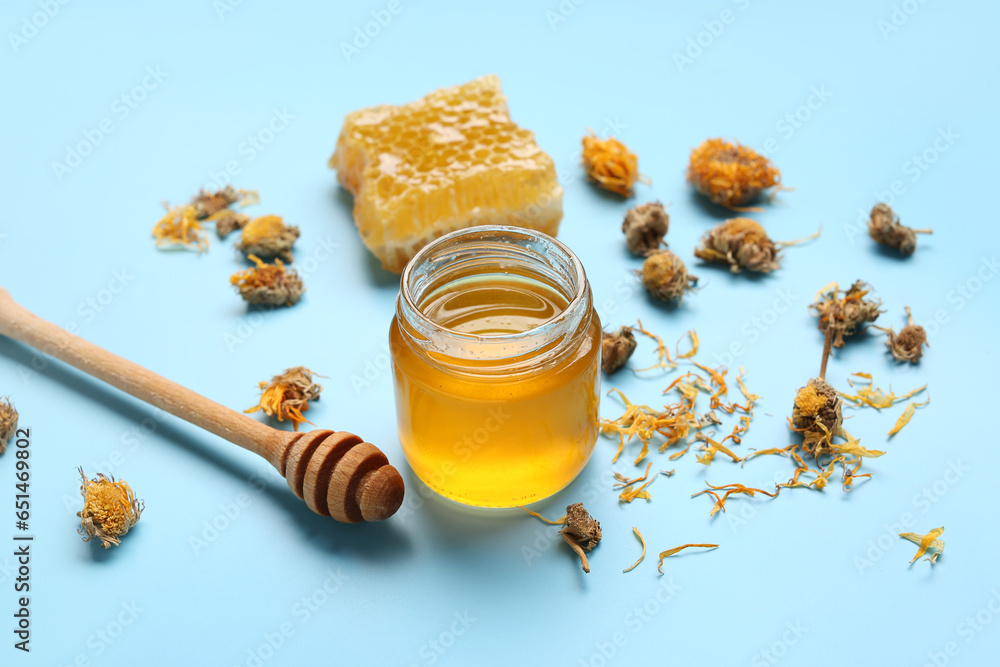 Jar with tasty honey, honeycomb, dipper and dried dandelion flowers on blue background, closeup