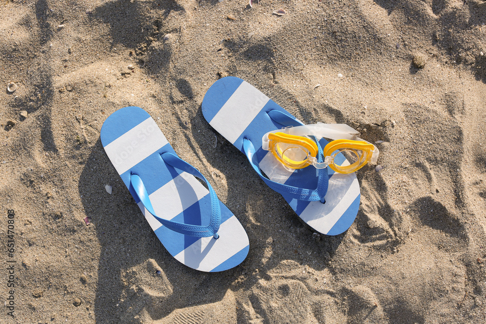 Stylish female blue flip flops and snorkeling mask on sand