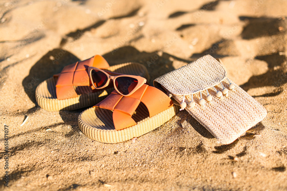 Stylish female flip flops, sunglasses and bag on sand, closeup