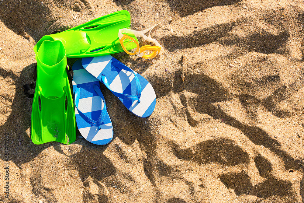 Stylish female blue flip flops, flippers and snorkeling mask on sand