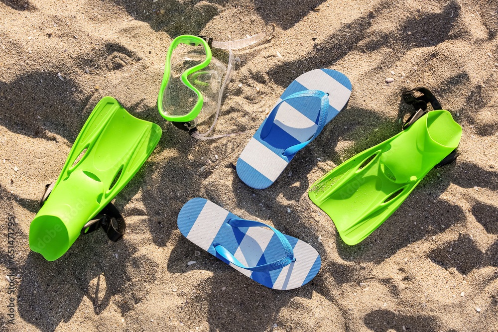 Stylish female blue flip flops, flippers and snorkeling mask on sand