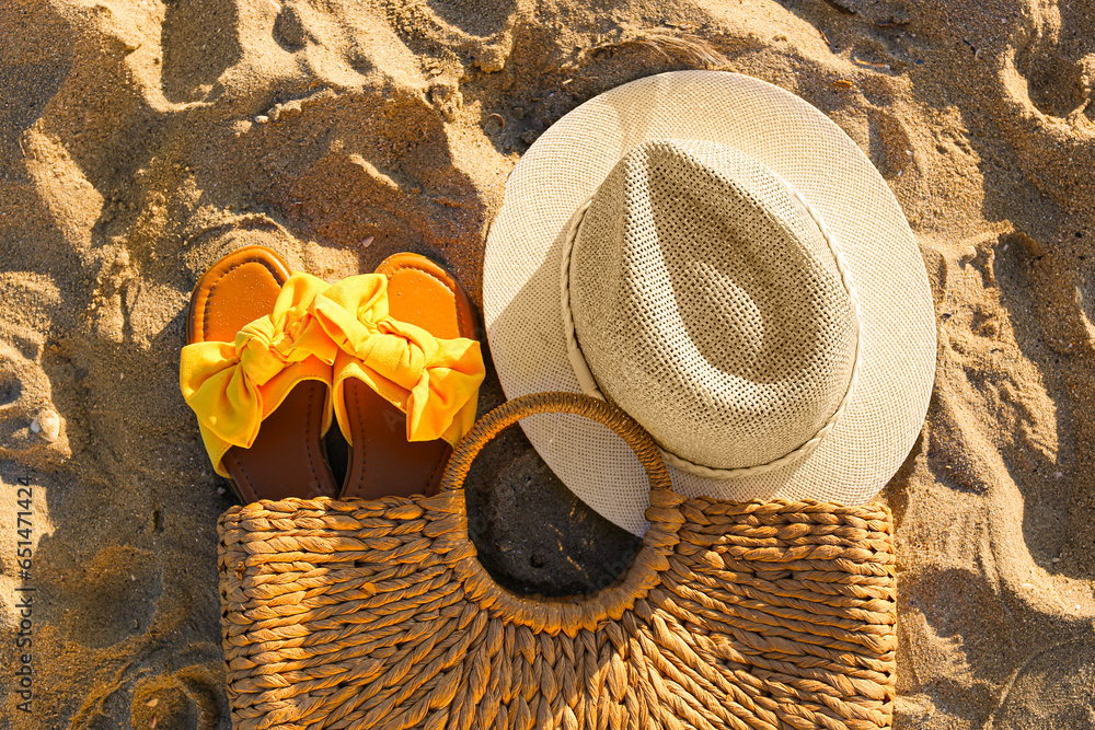 Stylish female flip flops, wicker bag and hat on sand