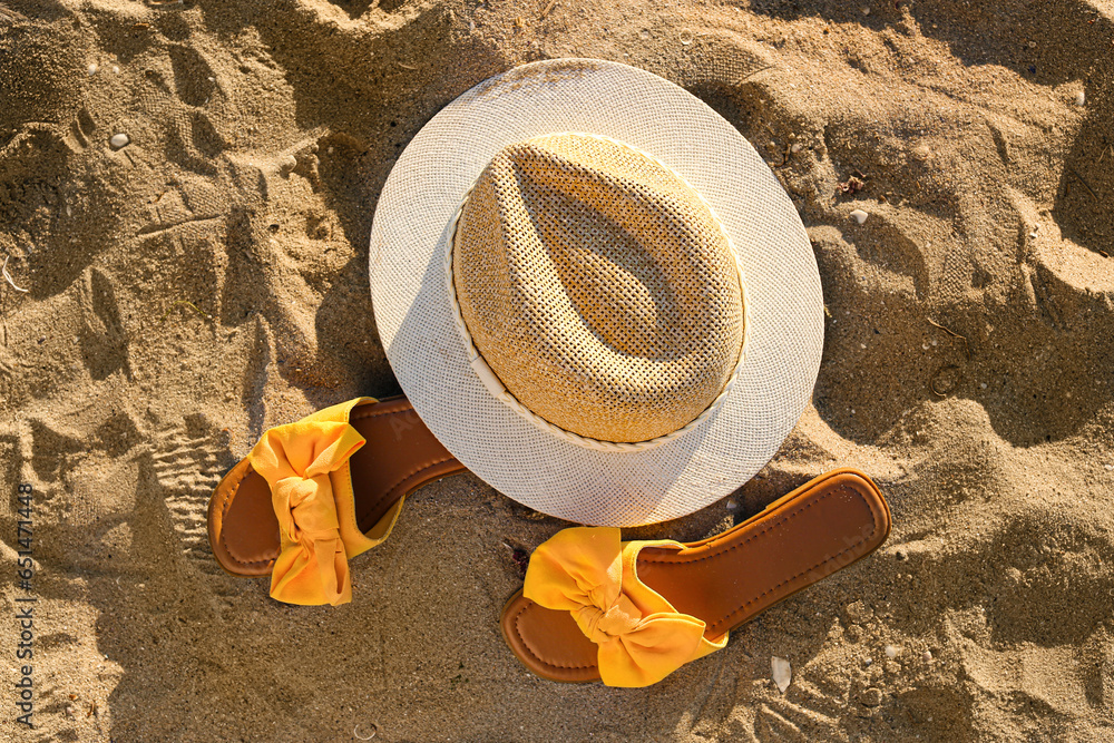 Stylish female flip flops and hat on sand