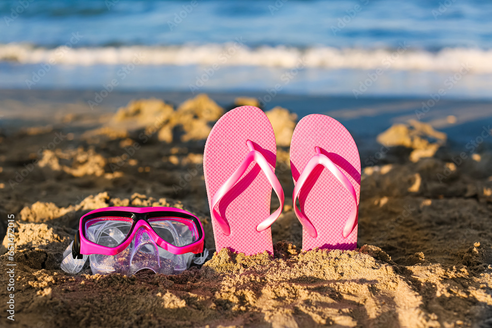 Stylish pink female flip flops and snorkeling mask on sand