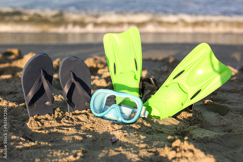 Stylish female flip flops, flippers and snorkeling mask on sand