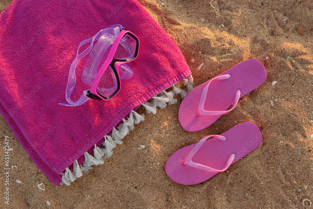 Stylish pink female flip flops, towel and snorkeling mask on sand