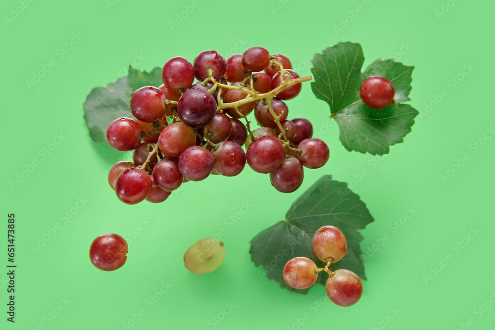 Tasty ripe grapes with leaves on green background