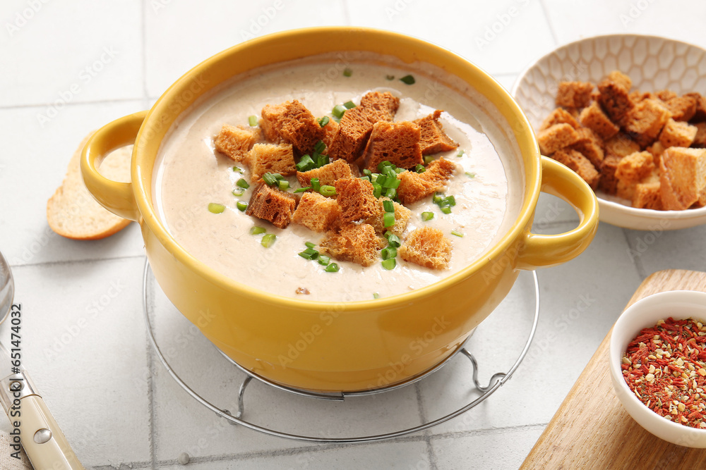 Pot of tasty cream soup with croutons on white tile background