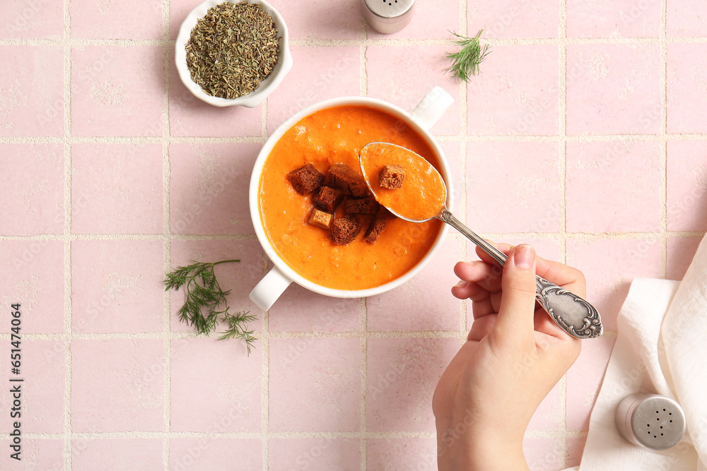 Woman eating tasty cream soup with croutons on pink tile background