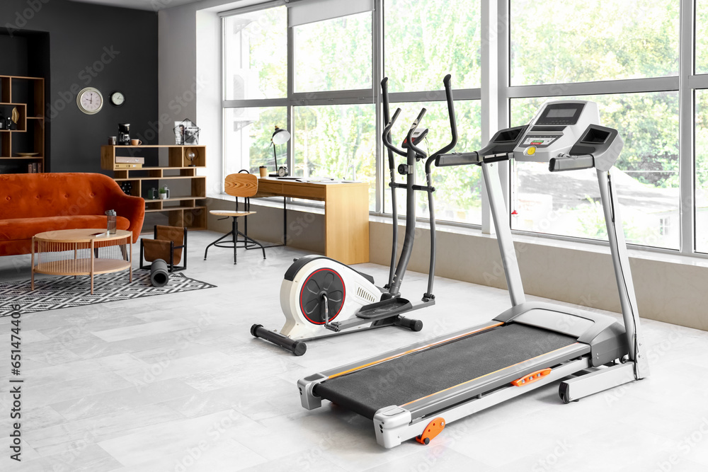 Interior of modern living room with workplace and sports equipment