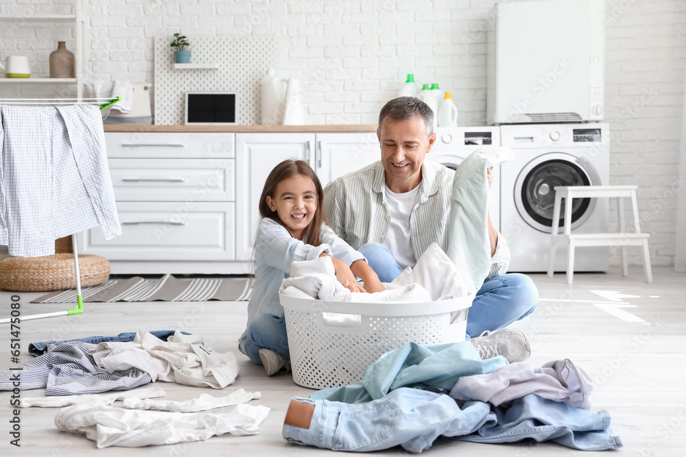 Mature man with his little granddaughter and dirty clothes in laundry room