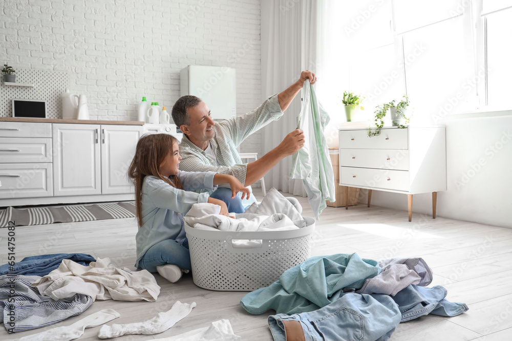 Mature man with his little granddaughter and dirty clothes in laundry room