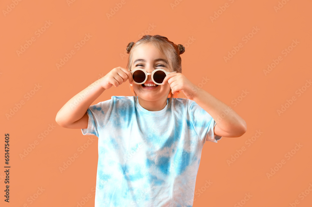 Cute little girl in sunglasses on orange background