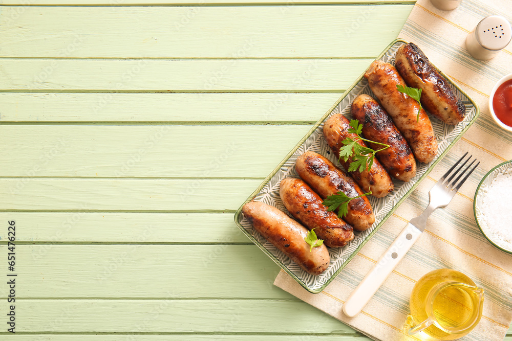 Plate of tasty grilled sausages on green wooden background