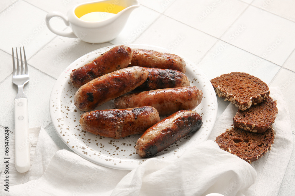 Plate of tasty grilled sausages and bread on white tile background