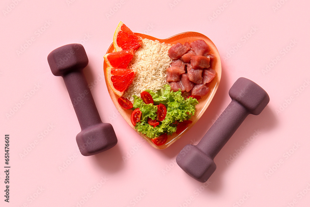 Plate with fresh healthy products and dumbbells on pink background. Diet concept