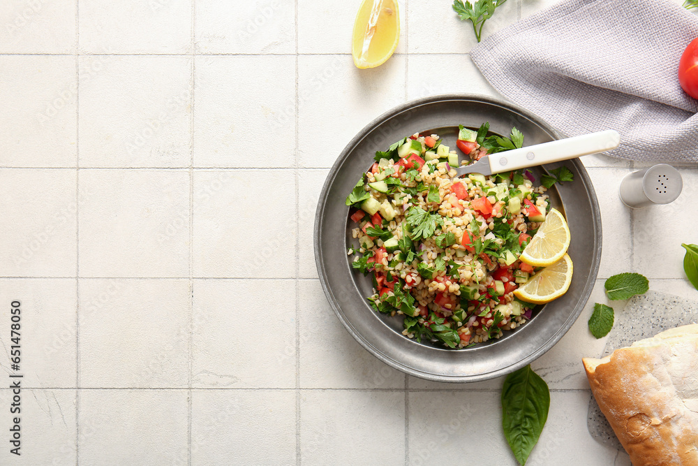 Plate with delicious tabbouleh salad and bread on light tile background