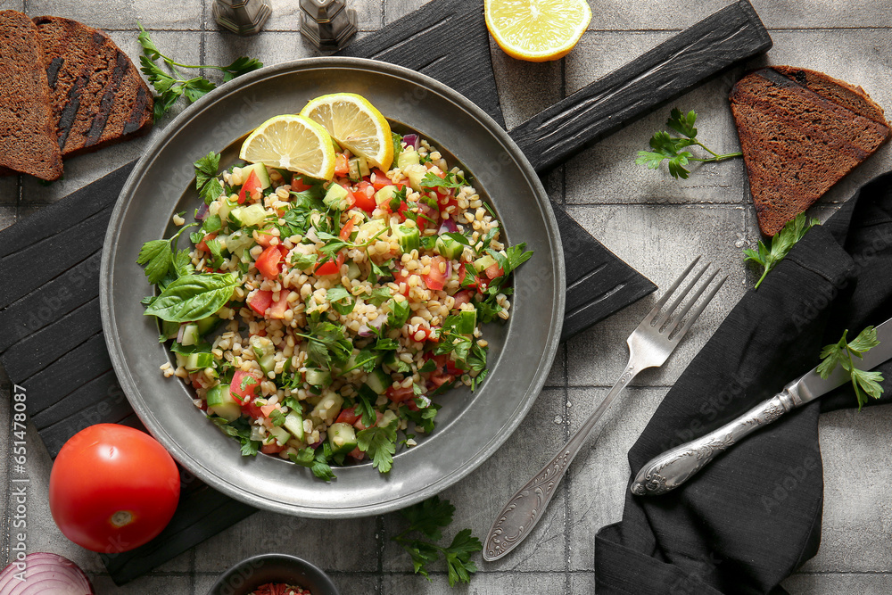 Plate with delicious tabbouleh salad on tile grey background