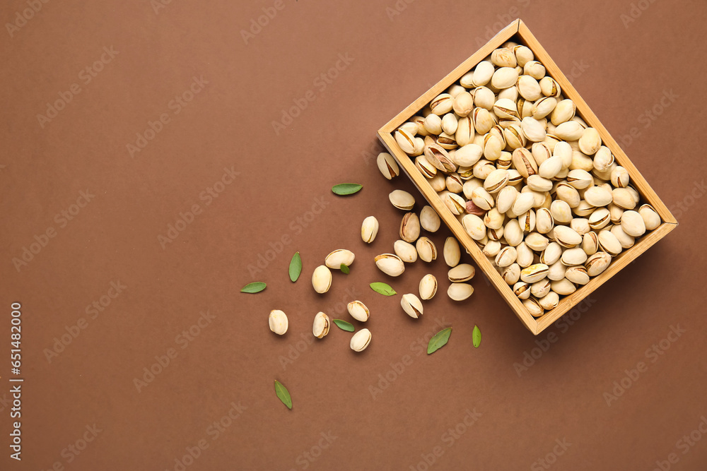 Wooden box with tasty pistachio nuts  and leaves on brown background