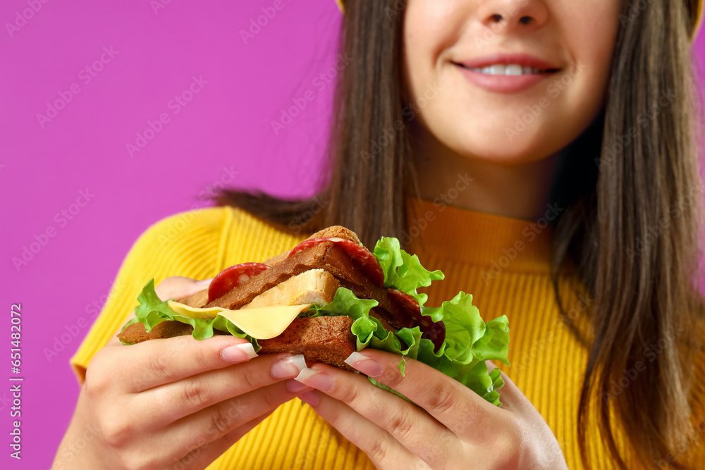 Young woman with tasty sandwich on purple background, closeup