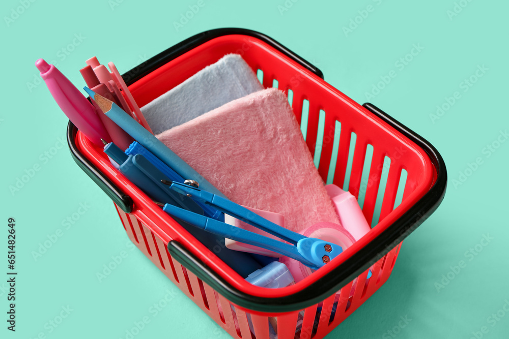 Shopping basket with different stationery on color background