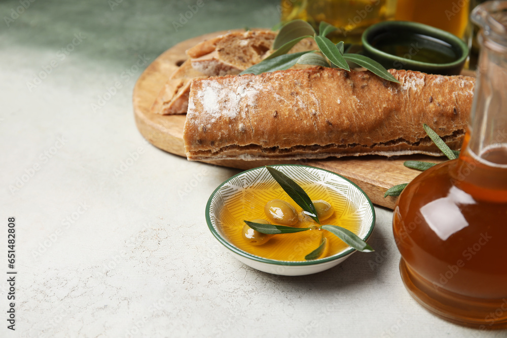 Bowl of fresh olive oil and bread on light background