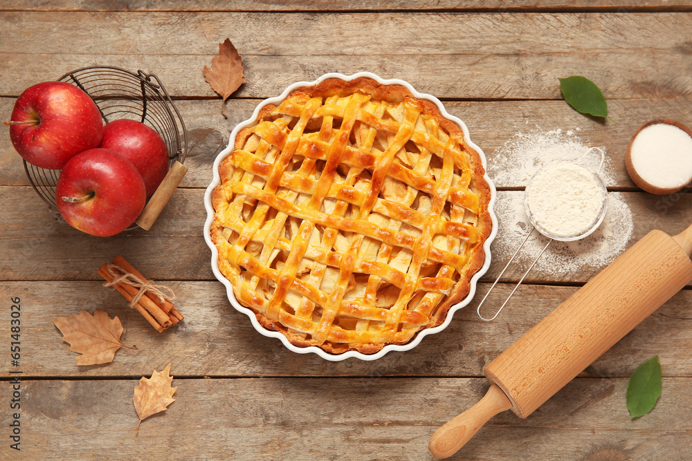 Baking dish with delicious apple pie and ingredients on wooden background