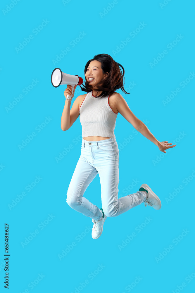 Jumping Asian woman with megaphone on blue background