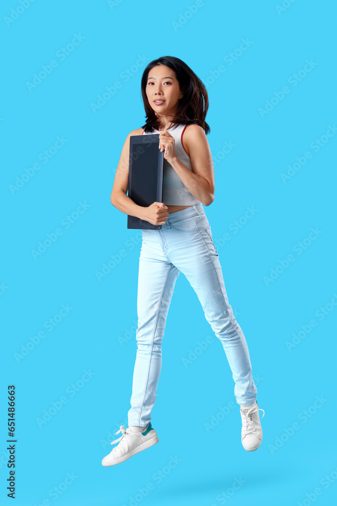 Jumping Asian woman with graphic tablet on blue background