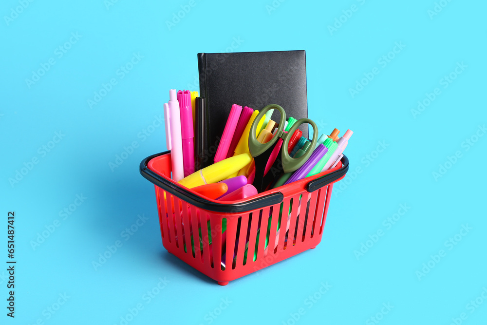 Red shopping basket with different school stationery on blue background