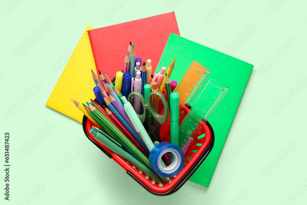 Shopping basket with different school stationery on green background