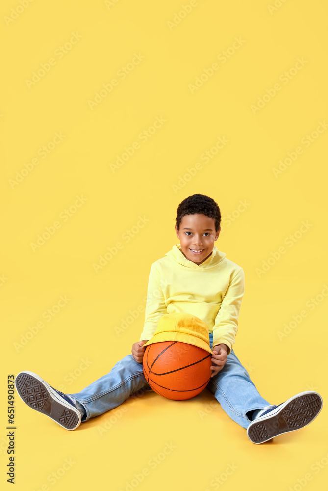 African-American little boy with ball sitting on yellow background