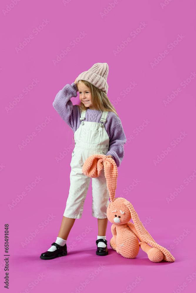 Cute little girl with toy bunny on purple background