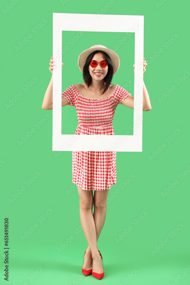 Stylish young beautiful Asian woman with frame on green background