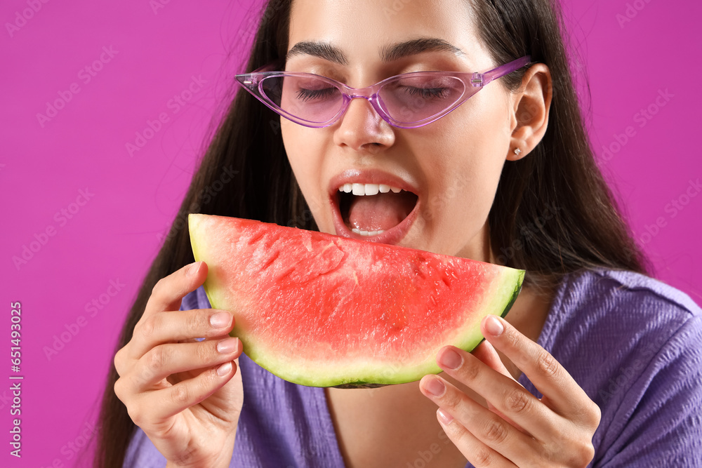 Beautiful young woman eating slice of fresh watermelon on purple background