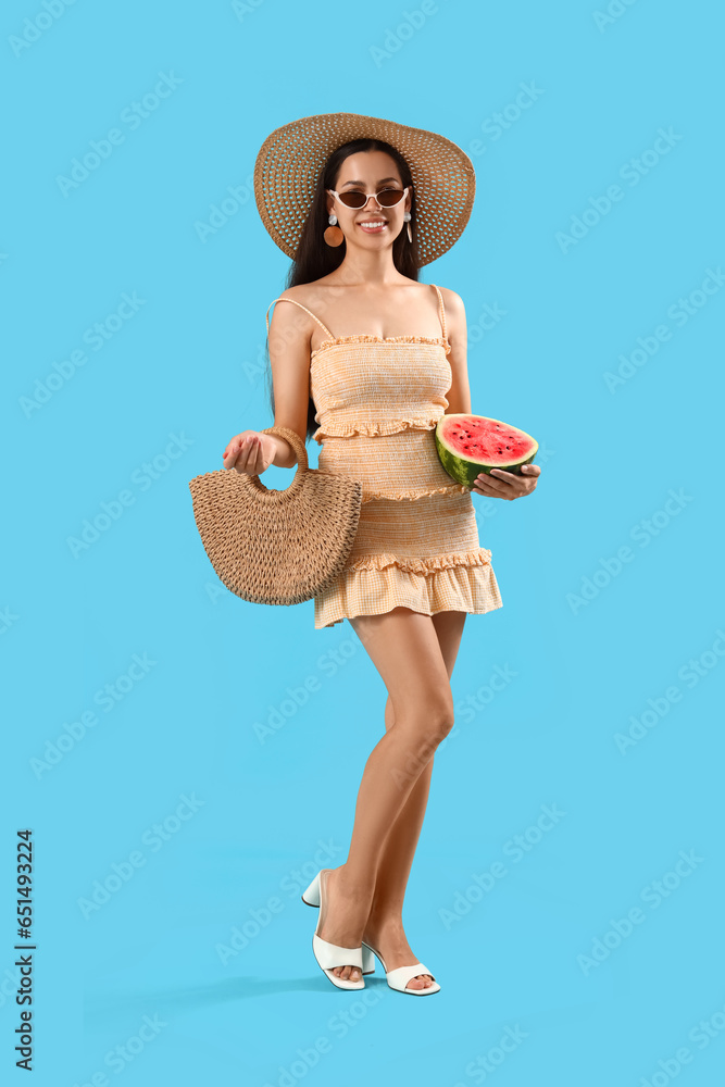 Beautiful young woman with wicker bag and half of fresh watermelon on blue background