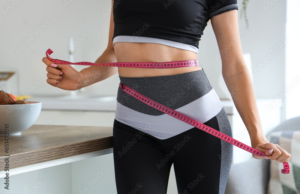 Beautiful young woman measuring her waist in kitchen. Weight loss concept