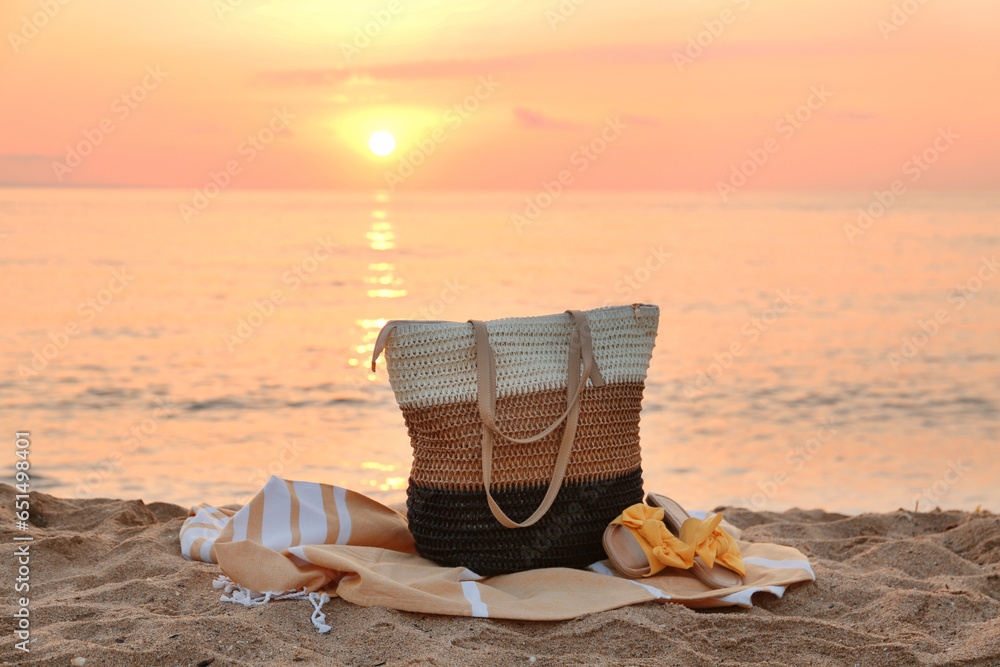 Stylish beach bag, towel and female shoes on sand near sea