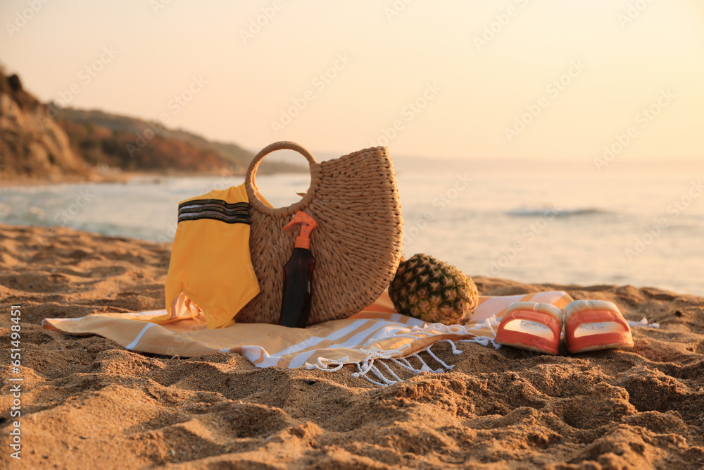 Stylish beach bag, flip-flops, pineapple, sunscreen spray, swimsuit and towel on sand near sea